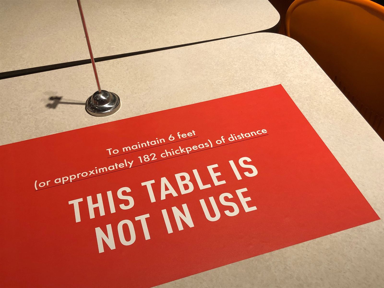 Red restaurant table sign: To maintain 6 feet (or approximately 182 chickpeas) of distance, this table is not in use